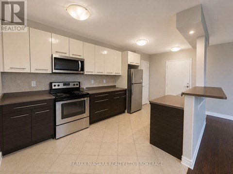 A kitchen with a stove top oven, microwave, refrigerator, and cabinets.