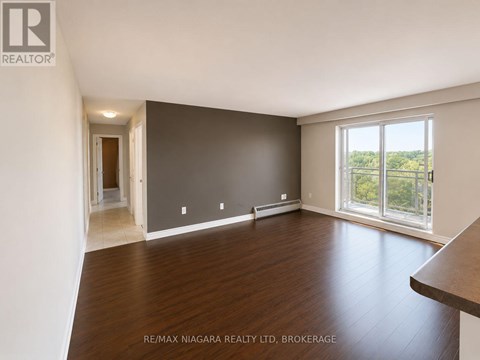 A spacious room with wooden flooring and a large window overlooking the outdoors.