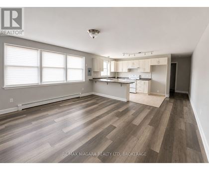A spacious room with wooden flooring and a kitchen area in the background.
