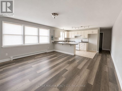 A spacious room with wooden flooring and a kitchen area in the background.