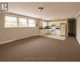 A spacious empty room with a kitchenette in the background.