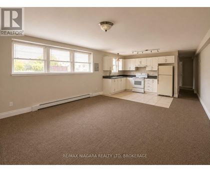 A spacious empty room with a kitchenette in the background.