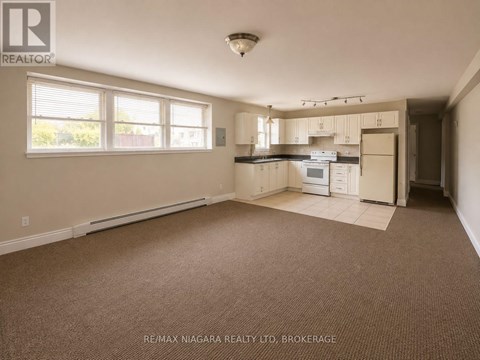 A spacious empty room with a kitchenette in the background.