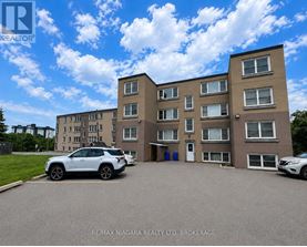 A white car is parked in front of a building with a sign that reads "RE/MAX NIAGARA REALTY LTD. BROKERAGE.".