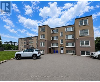 A white car is parked in front of a building with a sign that reads "RE/MAX NIAGARA REALTY LTD. BROKERAGE.".