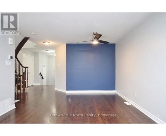 A spacious room with a staircase on the left and a ceiling fan above.