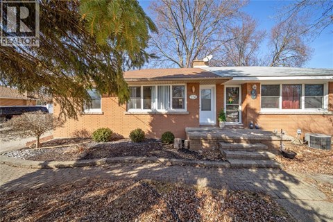 A house with a brown brick exterior and a white door is surrounded by a gravel driveway.