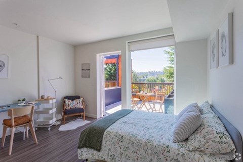 A bedroom with a bed, desk, chair, and a view of the backyard through the open door.