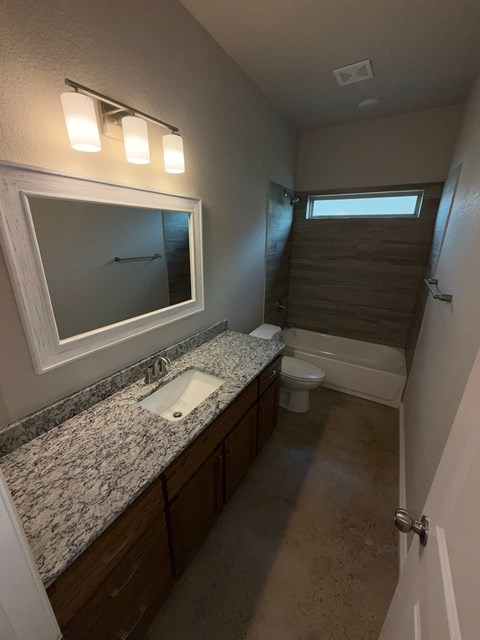 A bathroom with a sink, mirror, toilet, and a window.