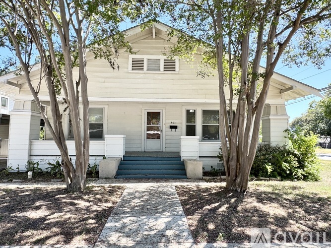 A white house with a front porch and two trees in front.