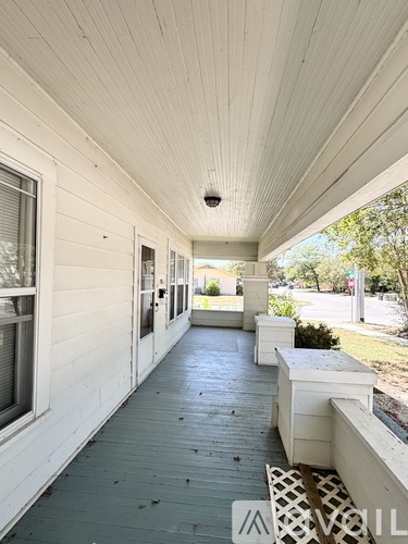 A long white porch with a white railing and a white bench.