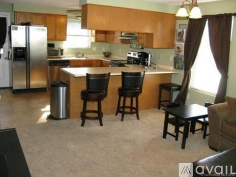 A kitchen with a refrigerator, sink, and bar stools.