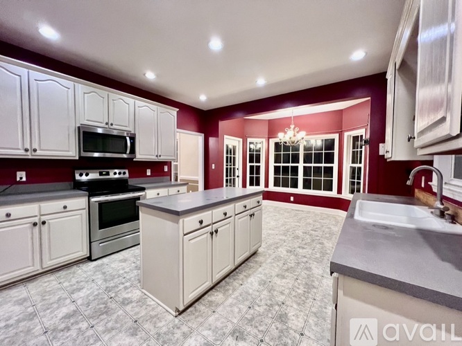 A kitchen with white cabinets and a maroon wall.