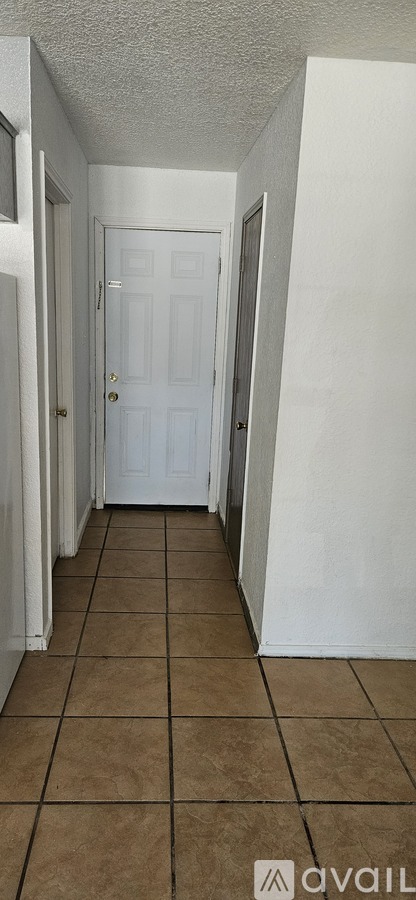 A hallway with a white door and brown tile flooring.