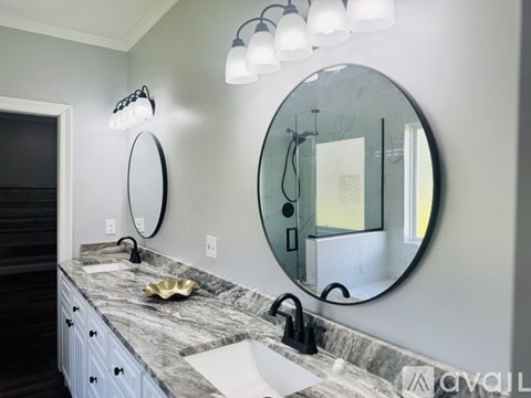 A bathroom with a marble countertop and a large round mirror.