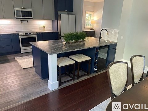 A kitchen with dark blue cabinets and a wooden island with three chairs.