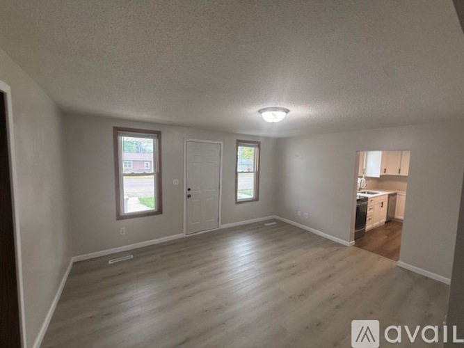 A spacious room with wooden flooring and two windows.