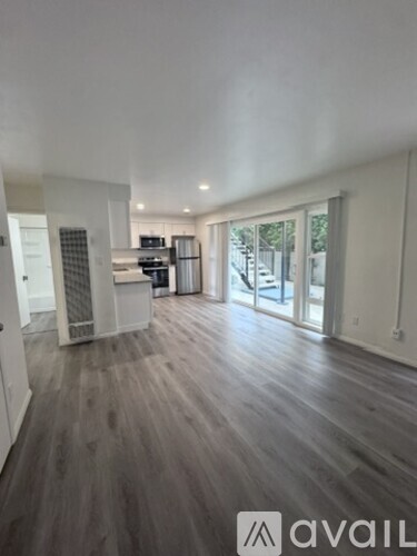 A spacious room with wooden flooring and a kitchen area in the background.
