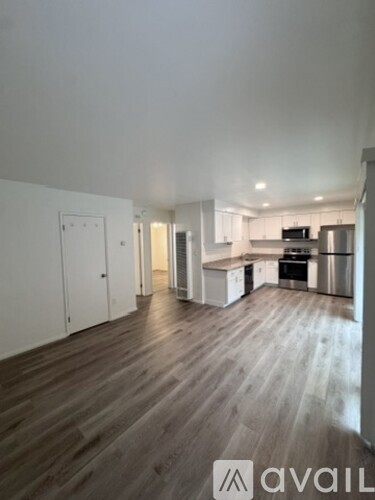 A room with wooden flooring and a kitchen area in the background.