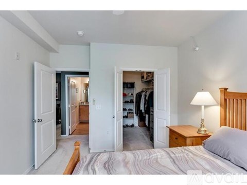 A bedroom with a bed, a nightstand with a lamp, and a closet with clothes.