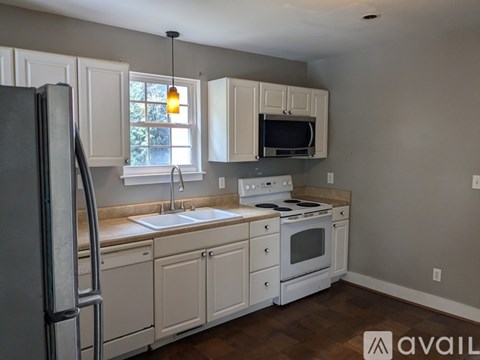 A kitchen with white cabinets and appliances, a window above the sink, and a wooden floor.