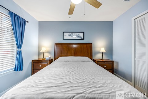 A bedroom with a bed, two lamps, and a ceiling fan.