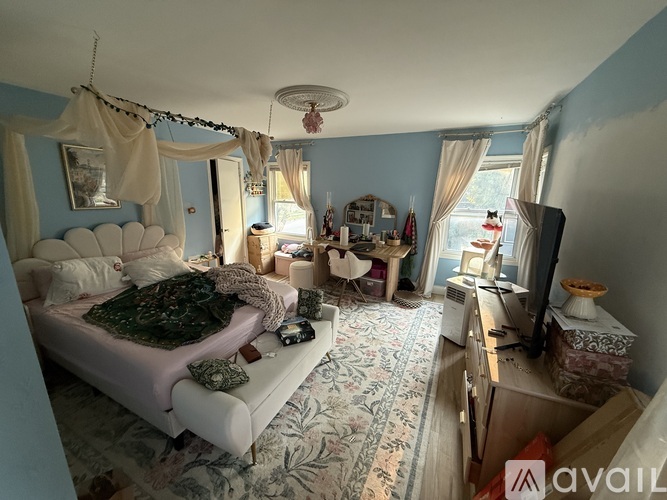 A bedroom with a bed, a couch, a rug, and a window with curtains.