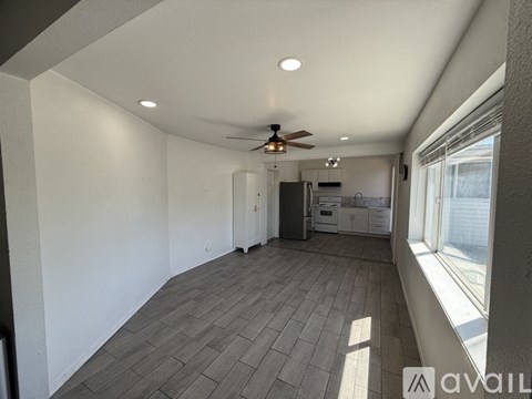 A spacious room with a ceiling fan and a kitchen area in the background.