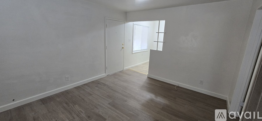 A room with wooden flooring and white walls, with a door leading to another room.