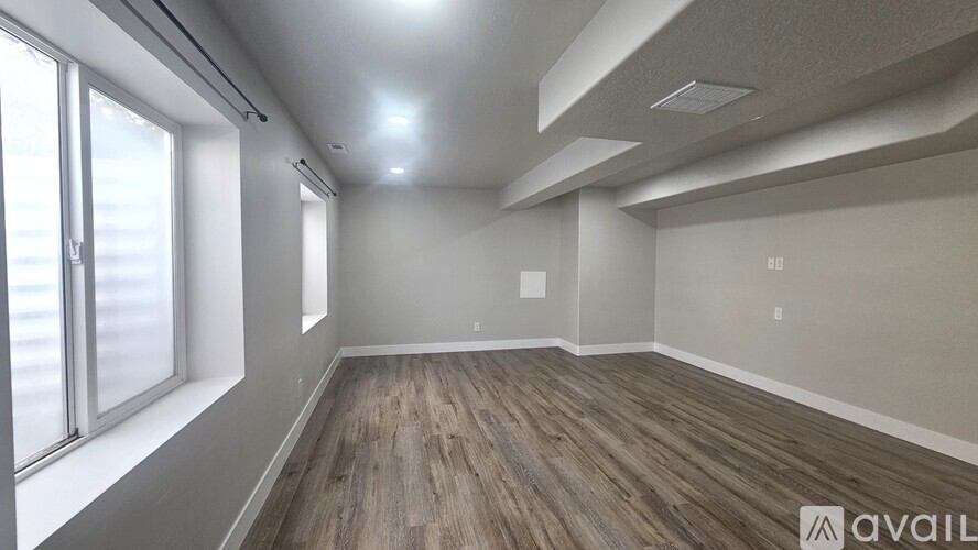 A spacious room with wooden flooring and large windows.