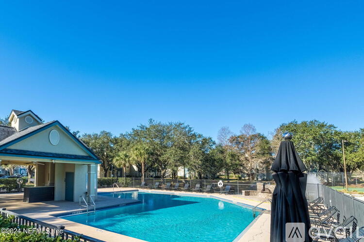A pool with a black umbrella and a small building in the background.