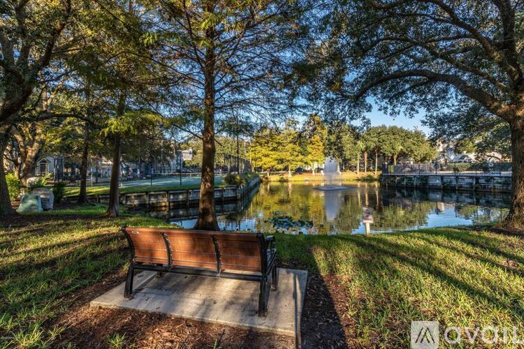 A park bench sits in front of a pond with trees in the background.