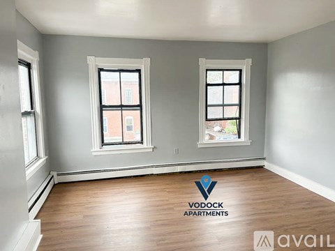 A room with wooden floors and two windows, one of which has a view of a building outside.