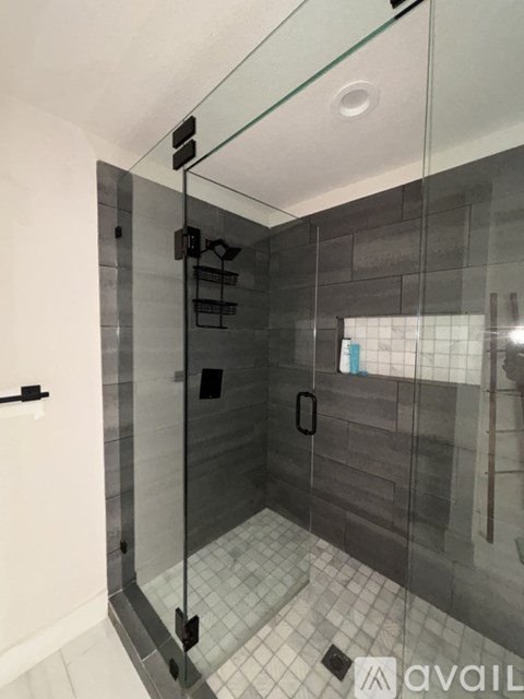 A glass shower stall with a glass door and a black handle.