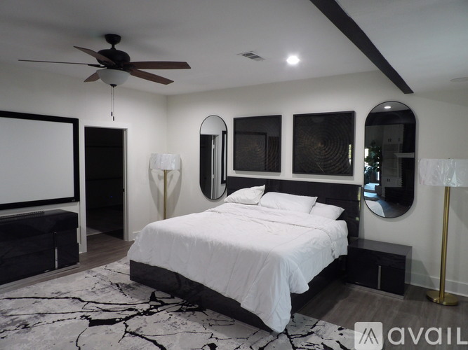 A bedroom with a large bed, a ceiling fan, and a mirror on the wall.
