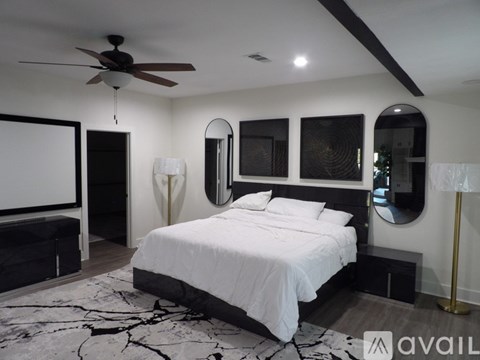 A bedroom with a large bed, a ceiling fan, and a mirror on the wall.