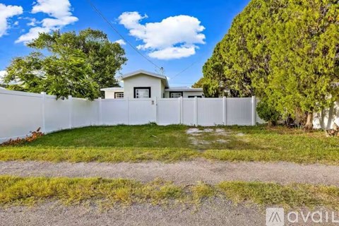 A house with a white fence and green trees in the background.