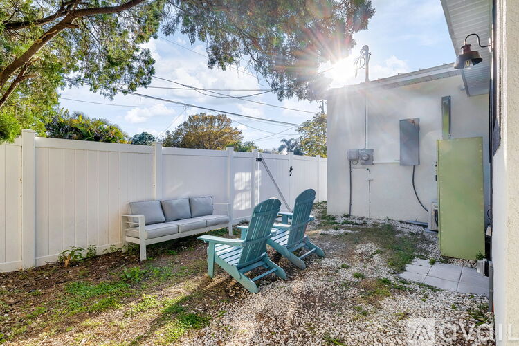 A sunny backyard with a white fence, a grey sofa, and green chairs.