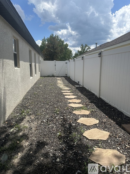 A white fence runs down a gravel path between two buildings.