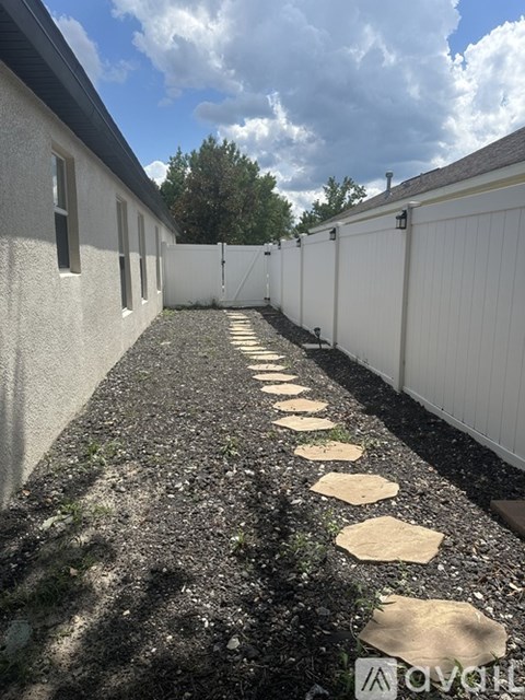 A white fence runs down a gravel path between two buildings.