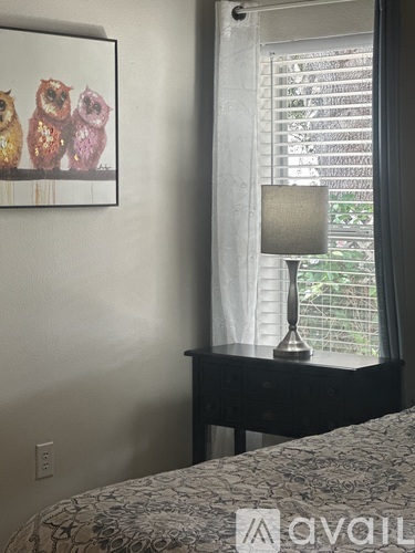 A bedroom with a bed, a nightstand with a lamp, and a picture of owls on the wall.