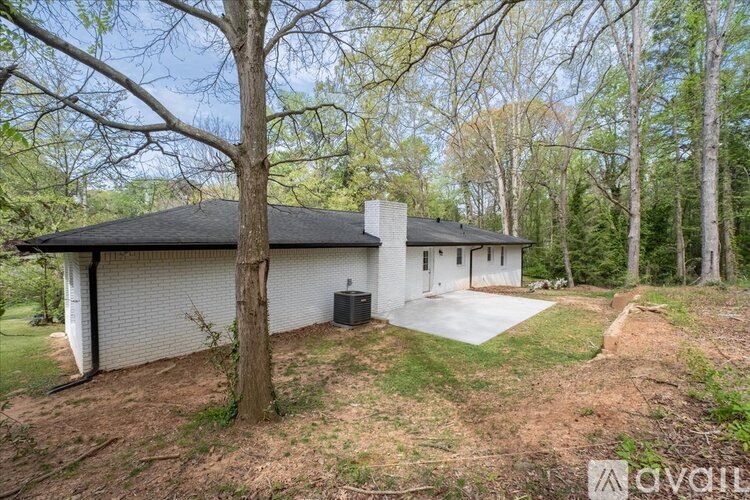 A house with a black roof is surrounded by trees and has a driveway leading to the garage.