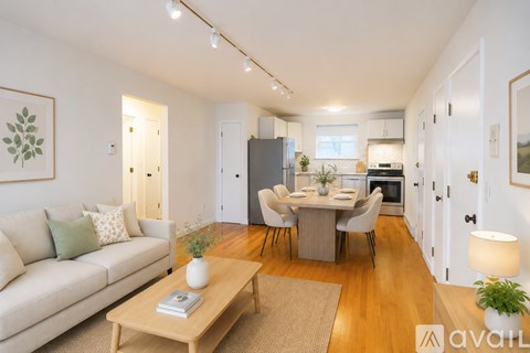 A well-lit living room with a couch, coffee table, and a dining area in the background.