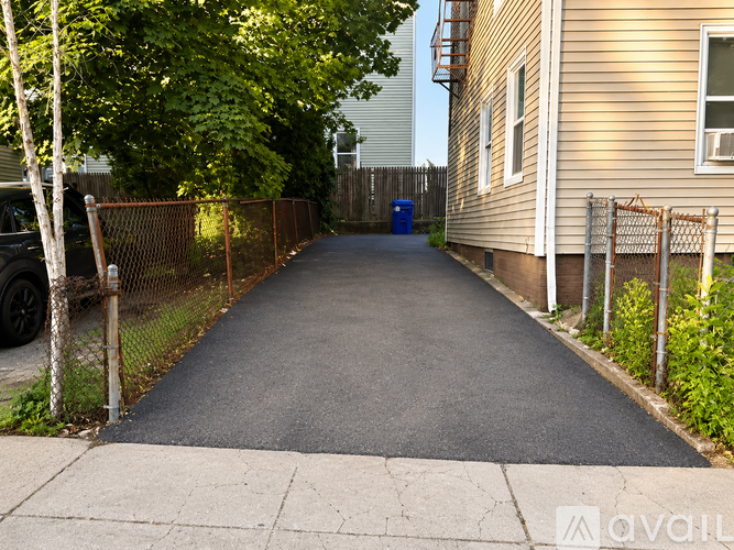 A long, narrow driveway leads to a house with a blue trash can in the middle.