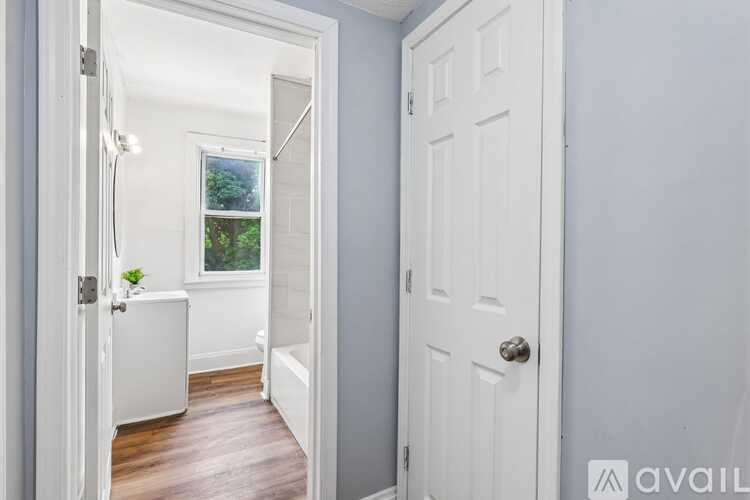 A white door is open to a bathroom with a tub and a window.