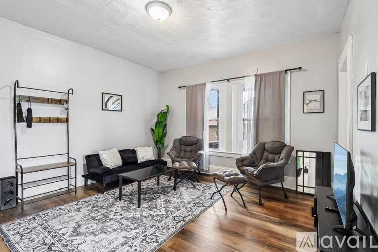 A living room with a black couch, a grey armchair, a black and white rug, and a wooden floor.
