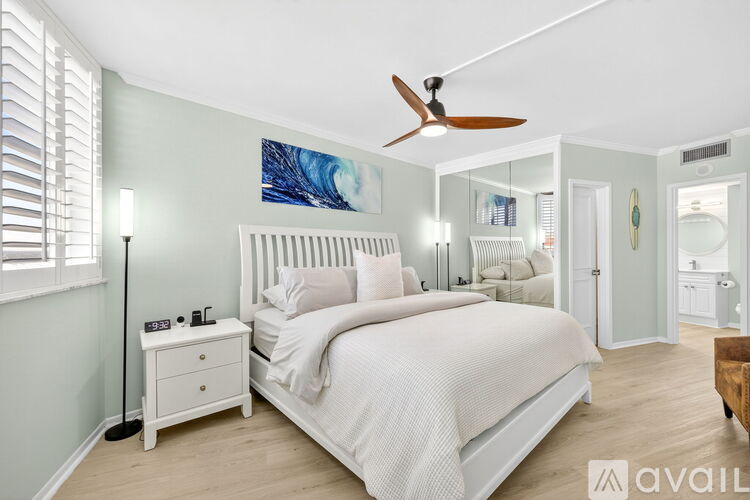 A bedroom with a large bed, a ceiling fan, and a nightstand with a lamp.