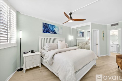 A bedroom with a large bed, a ceiling fan, and a nightstand with a lamp.
