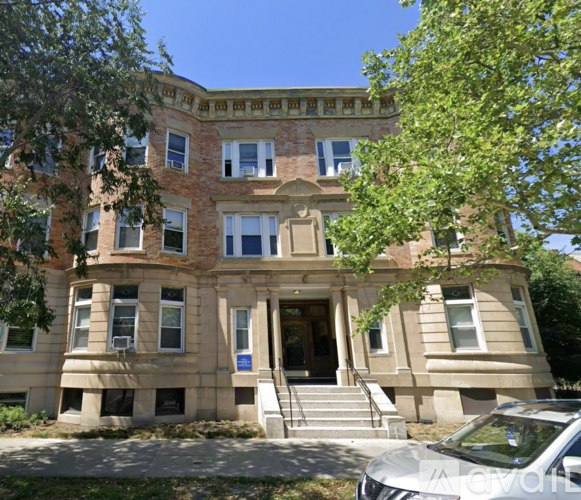 A large, two-story building with a beige facade and a blue sign on the front door.