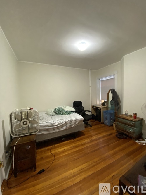 A room with a bed, a fan, and a chair.